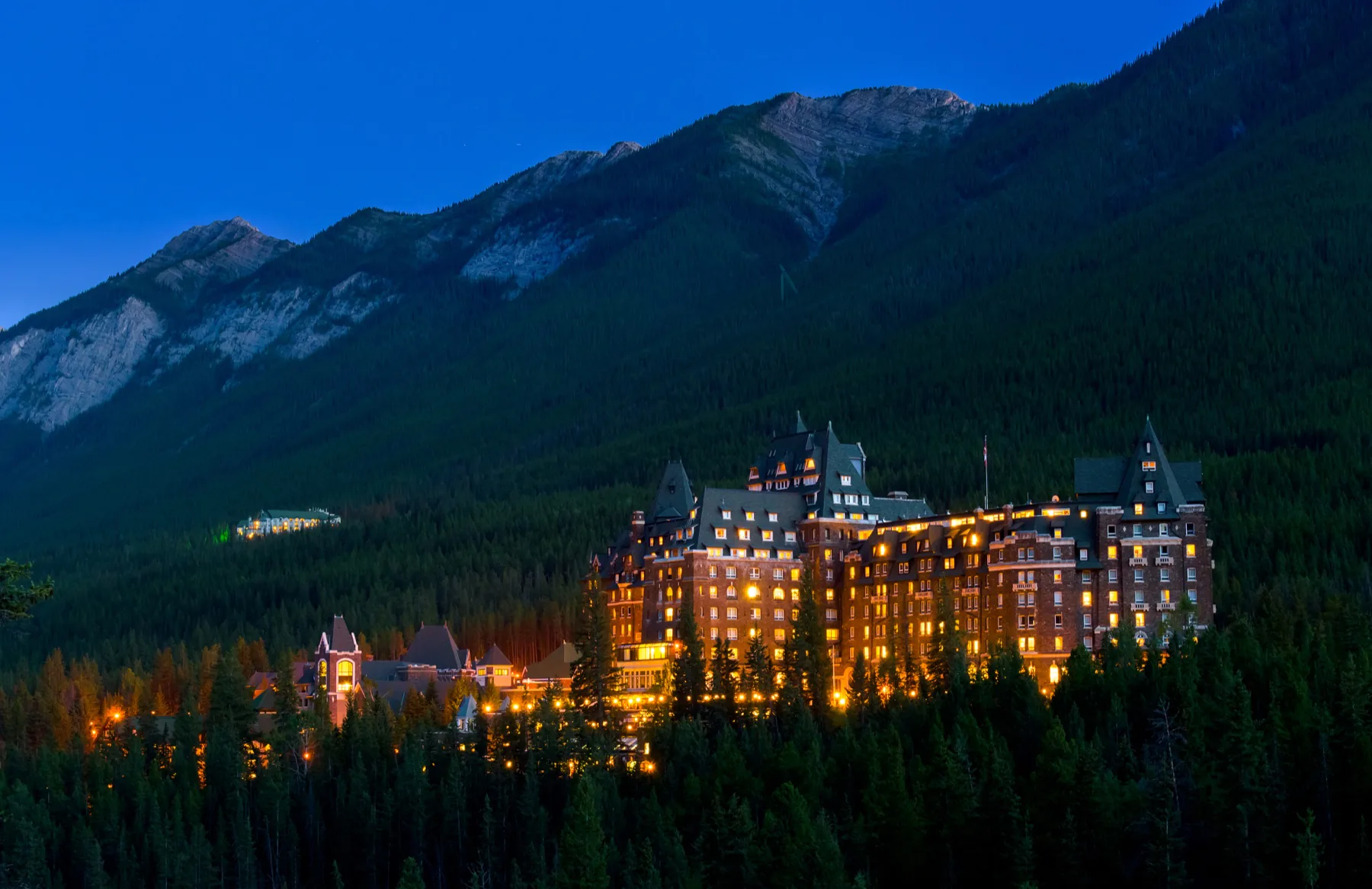 A grand illuminated hotel surrounded by forest and mountains in Banff